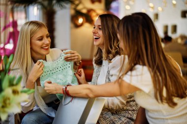 Üç mutlu genç kadın alışveriş yaptıktan sonra kafeteryada oturuyorlar ve siyah cuma günü satın aldıkları güzel şeylere bakıyorlar..