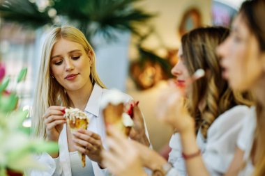Üç mutlu kız bir restoranda oturmuş alışveriş yaptıktan sonra sohbet ediyor ve dondurma yiyorlar..