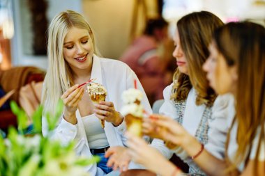 Üç mutlu kız bir restoranda oturmuş alışveriş yaptıktan sonra sohbet ediyor ve dondurma yiyorlar..