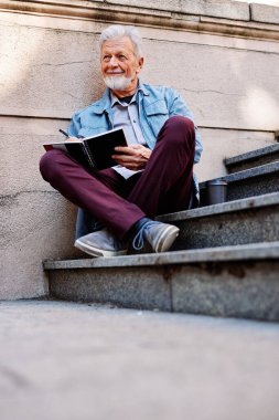 Mutlu bir son sınıf öğrencisi üniversite binasının önündeki merdivenlerde oturur ve ev ödevini yazar. Yaşlılar için geri çekilme programı.