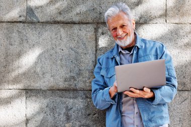Mutlu bir son sınıf öğrencisi tuğla duvarın önünde dizüstü bilgisayarda yazı yazıyor..