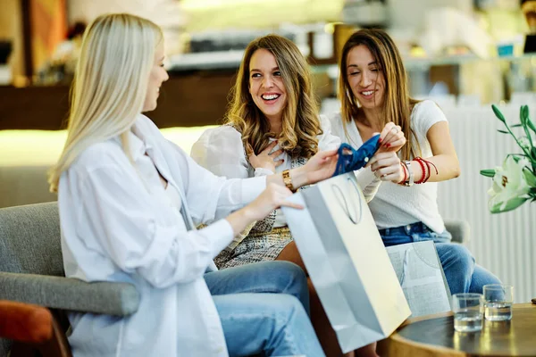 三个快乐的女孩坐在购物中心的自助餐厅里 看着她们在零售店里买的衣服 — 图库照片
