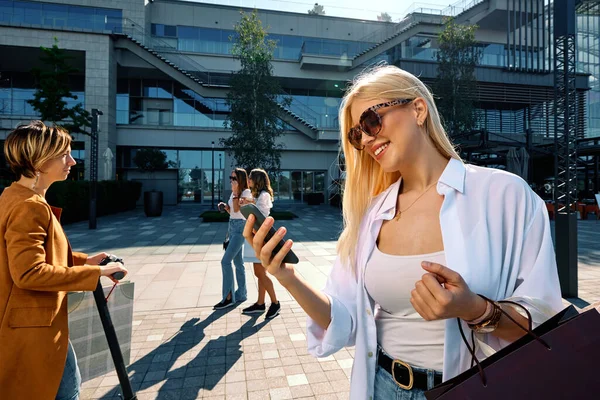 一个快乐的女人站在街上 手里拿着购物袋 用的是智能手机 购物后用电话的女人 — 图库照片