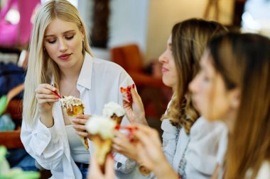 Üç mutlu kız bir restoranda oturmuş alışveriş yaptıktan sonra sohbet ediyor ve dondurma yiyorlar..