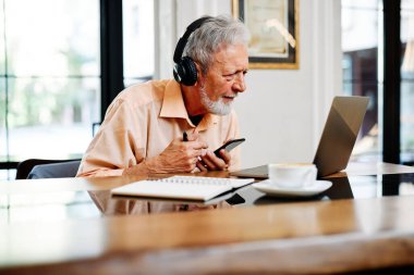 Kendini adamış bir son sınıf öğrencisi kafeteryada kulaklık takmış ve bilgisayarında online konferans dinliyor..