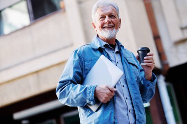 Mutlu bir son sınıf öğrencisi sokakta dizüstü bilgisayarını ve kahve fincanını tutuyor. Son sınıf öğrencisi bir konferansa gidiyor..