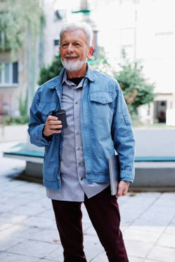 Mutlu bir son sınıf öğrencisi sokakta dizüstü bilgisayarını ve kahve fincanını tutuyor. Son sınıf öğrencisi bir konferansa gidiyor..