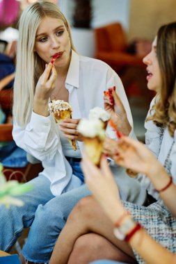 Üç mutlu kız bir restoranda oturmuş alışveriş yaptıktan sonra sohbet ediyor ve dondurma yiyorlar..