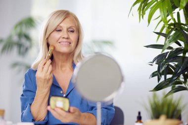 Güzel, sarışın, son sınıf öğrencisi bir kadın evde oturuyor ve sabah makyajını yapıyor. Kıdemli kadın yüzünü kızartıyor.