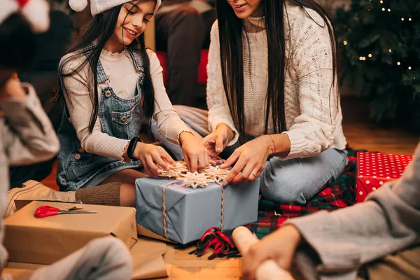 Mutlu kız Noel ağacının önünde annesiyle oturuyor ve Noel hediyesini açıyor..