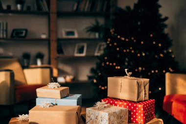 Noel hediyeleri, karanlık oturma odasındaki Noel ağacının önünde ambalaj kağıdına sarılı..