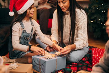 Mutlu bir anne ve kız evde yerde oturuyor ve Noel arifesinde hediyelerini açıyorlar..