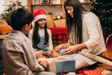Bir anne küçük yardımcılarıyla Noel hediyelerini paketliyor..