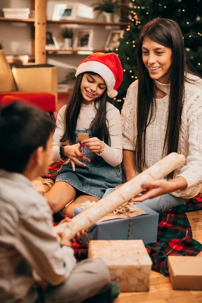 Mutlu bir aile yerde birlikte oturur ve Noel arifesinde Noel hediyelerini paketler..