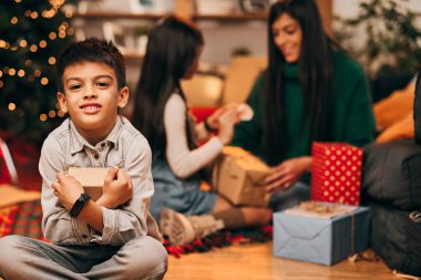 Evde oturup istediği Noel hediyesini kucaklayan tatlı bir çocuk. Yeni yıl ve Noel tatili konsepti.