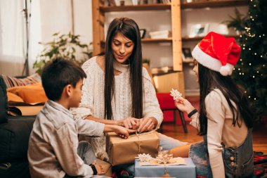 Mutlu bir aile yerde birlikte oturur ve Noel arifesinde Noel hediyelerini paketler..
