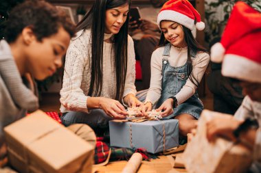 Mutlu bir aile yerde birlikte oturur ve Noel arifesinde Noel hediyelerini paketler..