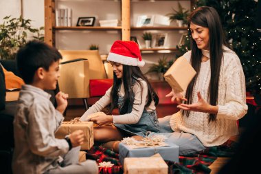 Mutlu bir aile yerde birlikte oturur ve Noel arifesinde Noel hediyelerini paketler..