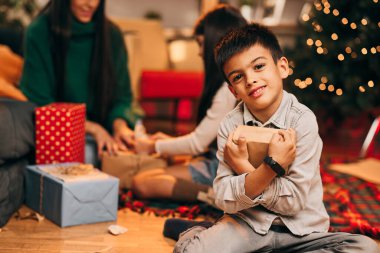 Evde oturup istediği Noel hediyesini kucaklayan tatlı bir çocuk. Yeni yıl ve Noel tatili konsepti.
