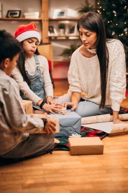 Mutlu bir aile yerde birlikte oturur ve Noel arifesinde Noel hediyelerini paketler. Noel ve Yeni Yıl
