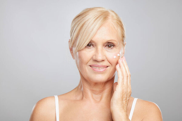 An attractive blond senior woman putting anti-age creme. Beauty photography