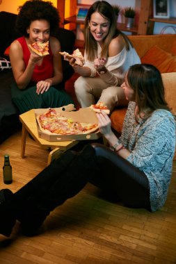 Mutlu çok kültürlü bayan arkadaşlar evde parti veriyor ve pizza yiyorlar..