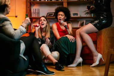 Mutlu çok kültürlü arkadaşlar evde oturup gülüyor, şarkı söylüyor ve karaoke gecesinde eğleniyorlar..