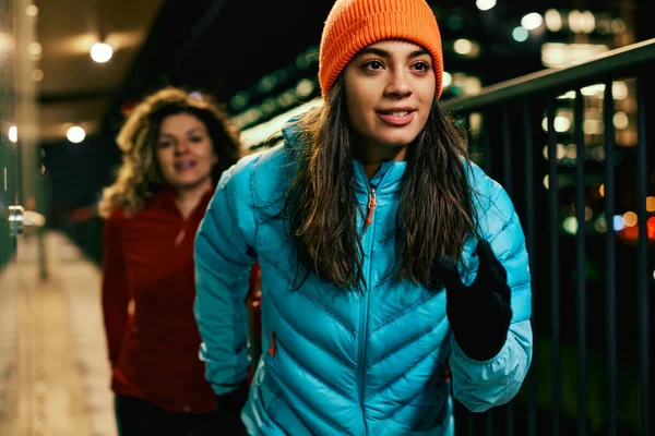Fit night runner in warm outfit running on the street and running with a friend.