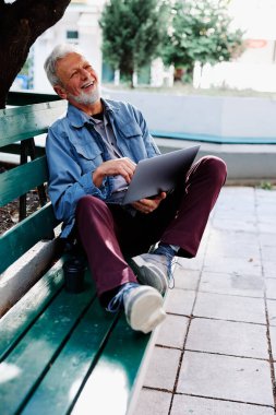 Mutlu bir son sınıf öğrencisi parkta bankta oturur ve dizüstü bilgisayarını kucağında tutar. Eğitimdeki son sınıf öğrencileri.