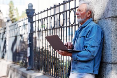 Bir son sınıf öğrencisi elinde dizüstü bilgisayarla üniversitesinin önünde duruyor ve test sonuçlarını kontrol ediyor. Eğitimdeki son sınıflar.