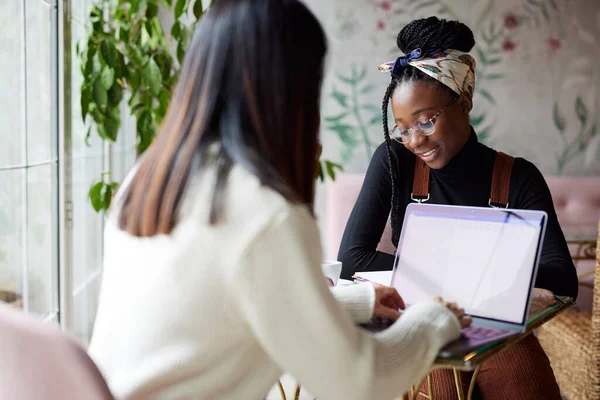İki mutlu çok kültürlü üniversiteli kız kafeteryada oturuyor ve bir okul projesi üzerinde çalışıyor. Yüksek öğrenim.