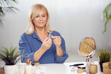 Güzel sarışın, son sınıf öğrencisi bir kadın evde oturuyor ve dudaklarına ruj sürüyor..