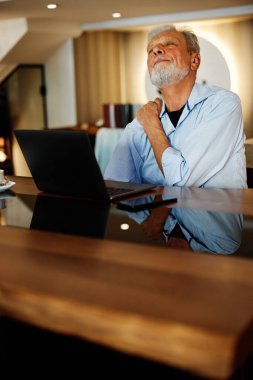 Bir son sınıf öğrencisi evde oturuyor ve omzunu ovuyor. Oturup ders çalışmaktan yoruldu..