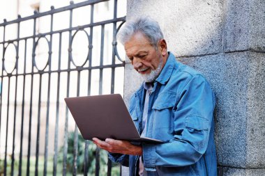 Bir son sınıf öğrencisi elinde dizüstü bilgisayarla üniversitesinin önünde duruyor ve test sonuçlarını kontrol ediyor. Eğitimdeki son sınıflar.