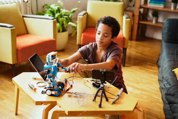一个聪明的非裔美国男孩拿着焊铁和触控板 同时在家里制造机器人 电子教育 — 图库照片