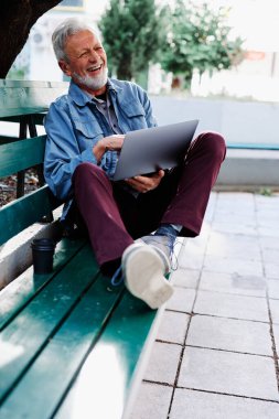 Mutlu bir son sınıf öğrencisi parkta bankta oturur ve dizüstü bilgisayarını kucağında tutar. Eğitimdeki son sınıf öğrencileri.