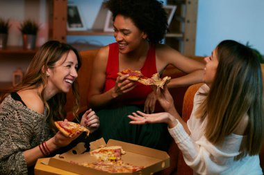 Mutlu çok kültürlü bayan arkadaşlar evde parti veriyor ve pizza yiyorlar..