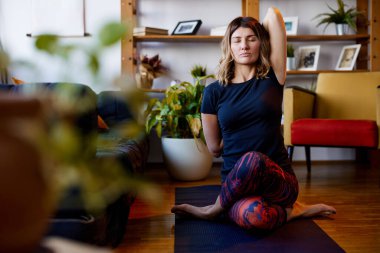 Esnek bir kadın evde yoga minderinde oturuyor. Ayakkabı bağcığı yoga duruşu ve meditasyon..