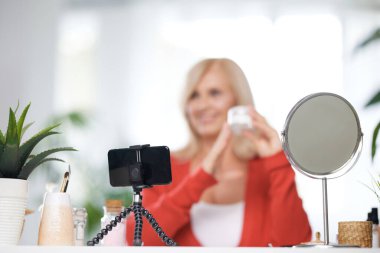 Yaşlı bir vlogger evde oturup yeni anti-yaş kreminden bahsediyor. Telefona odaklan..