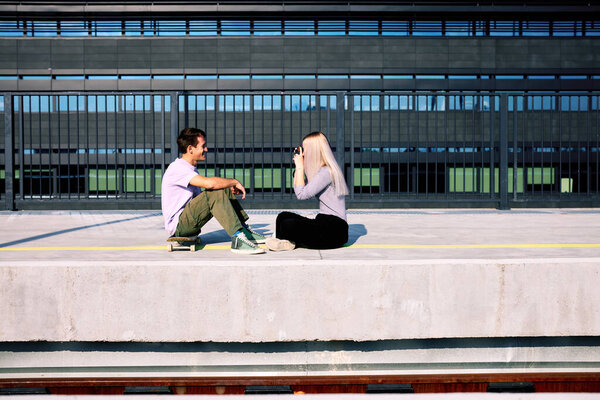 A happy teenage couple is sitting at the train station and taking photos.