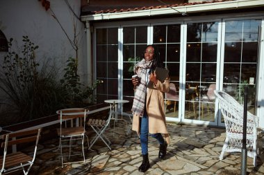 Kafe terasında elinde laptopla gezen mutlu bir Afrikalı kadın. Uzak ve serbest çalışma.