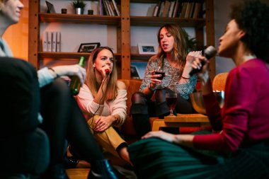 Mutlu çok kültürlü arkadaşlar evde oturup gülüyor, şarkı söylüyor ve karaoke gecesinde eğleniyorlar..