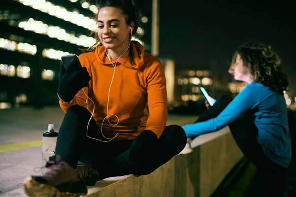 Усміхнена Спортсменка Сидить Вулиці Вночі Розслабляється Використовує Телефон — стокове фото