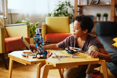 Evde robot yaparken lehim aleti tutan ve tablete dokunan zeki bir Afro-Amerikalı çocuk. Elektronik eğitimi.