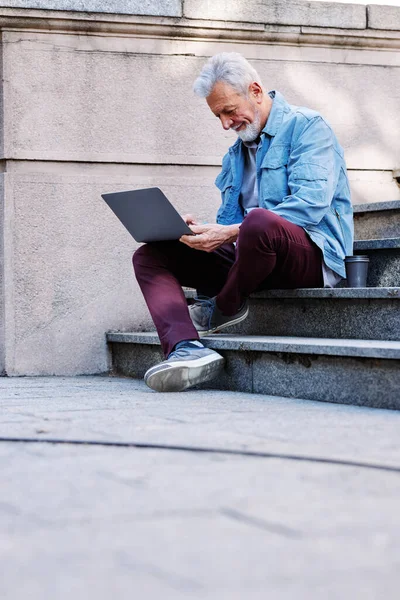 Son sınıf öğrencisi üniversite binasının merdivenlerinde oturur ve sınavdan önce bilgisayarını kullanarak notlara bakar..