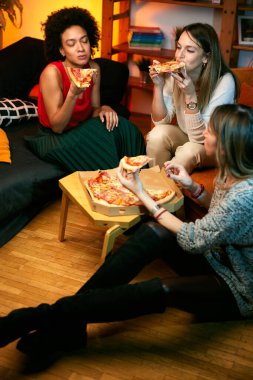 Mutlu çok kültürlü bayan arkadaşlar evde parti veriyor ve pizza yiyorlar..