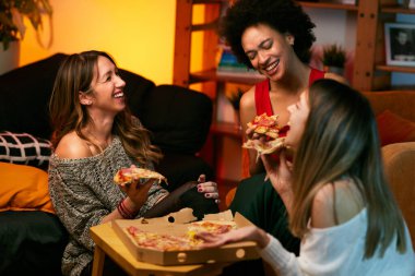 Mutlu çok kültürlü bayan arkadaşlar evde parti veriyor ve pizza yiyorlar..