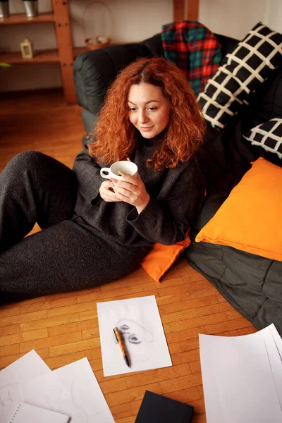 一个快乐可爱的姜汁女孩 卷曲的头发 手里拿着一杯咖啡 坐在家里的地板上 — 图库照片