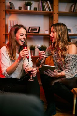 İki gülümseyen kız şarkı söylüyor ve evde karaoke yapıyorlar.