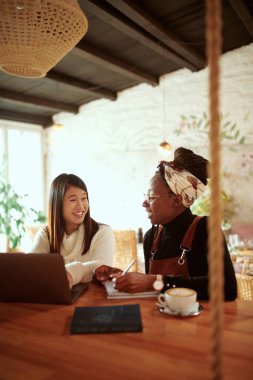 İki güzel çok kültürlü kız öğrenci bir kafede oturuyor ve dizüstü bilgisayardan konferans izliyorlar. Eğitimde teknoloji.